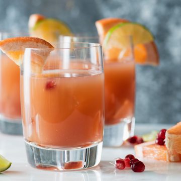 Close up of Pomegranate Paloma cocktail with two cocktails in background