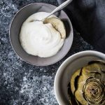 Artichoke dipping sauce with steamed artichoke on a grey background