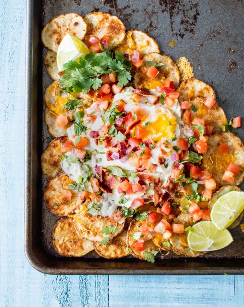 Crisp potato rounds topped with cheese, egg, tomatoes and cilantro on an old sheet pan