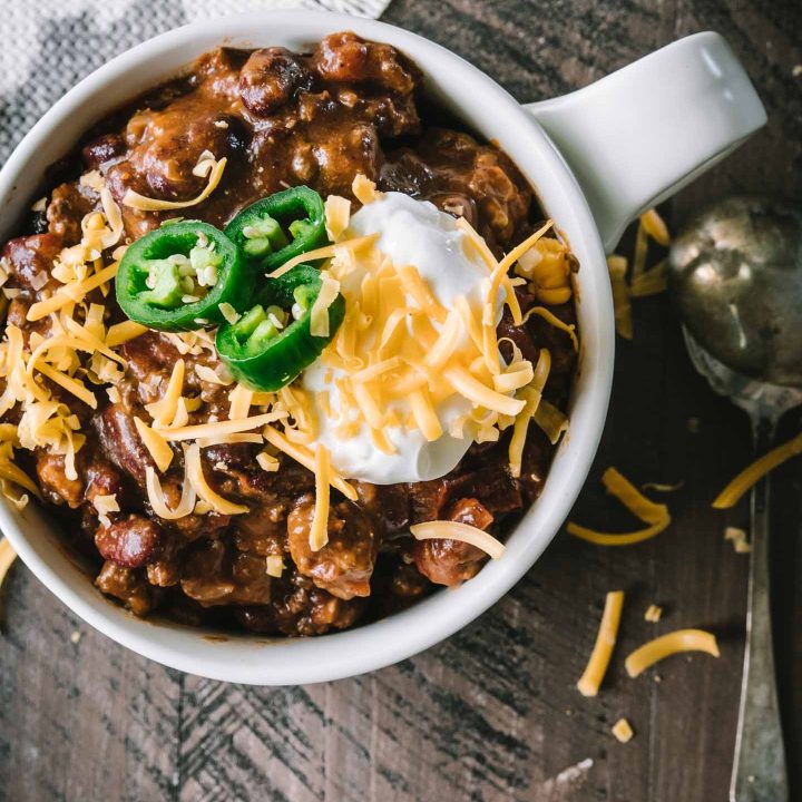 Beef chili topped with sour cream and shredded cheddar photographed from overhead
