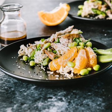 Ramen cakes topped with an Asian chicken salad with mandarin orange slices on a black plate