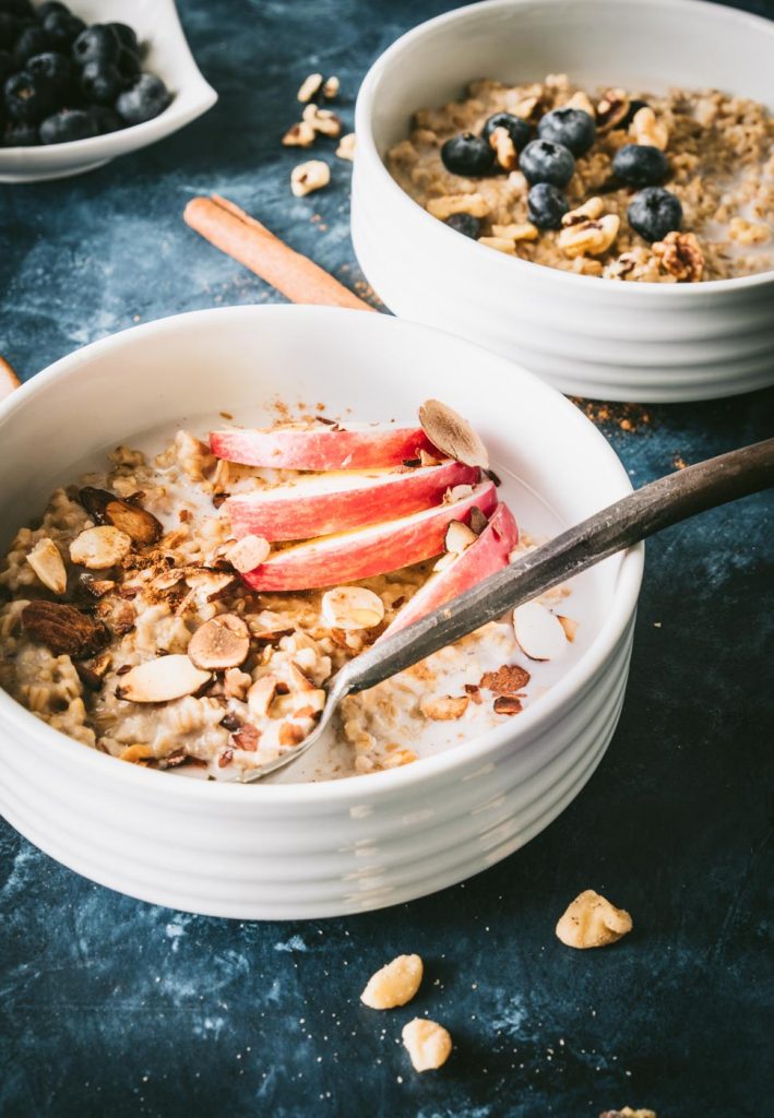 Steel cut oats in a white bowl topped with apple slices and almonds