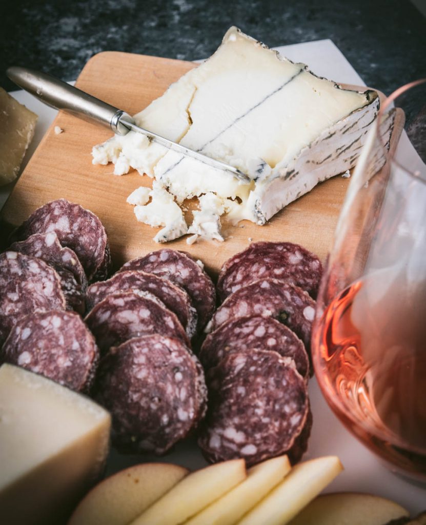 Truffle Tremor cheese on a wood board with salami and a glass of Rose