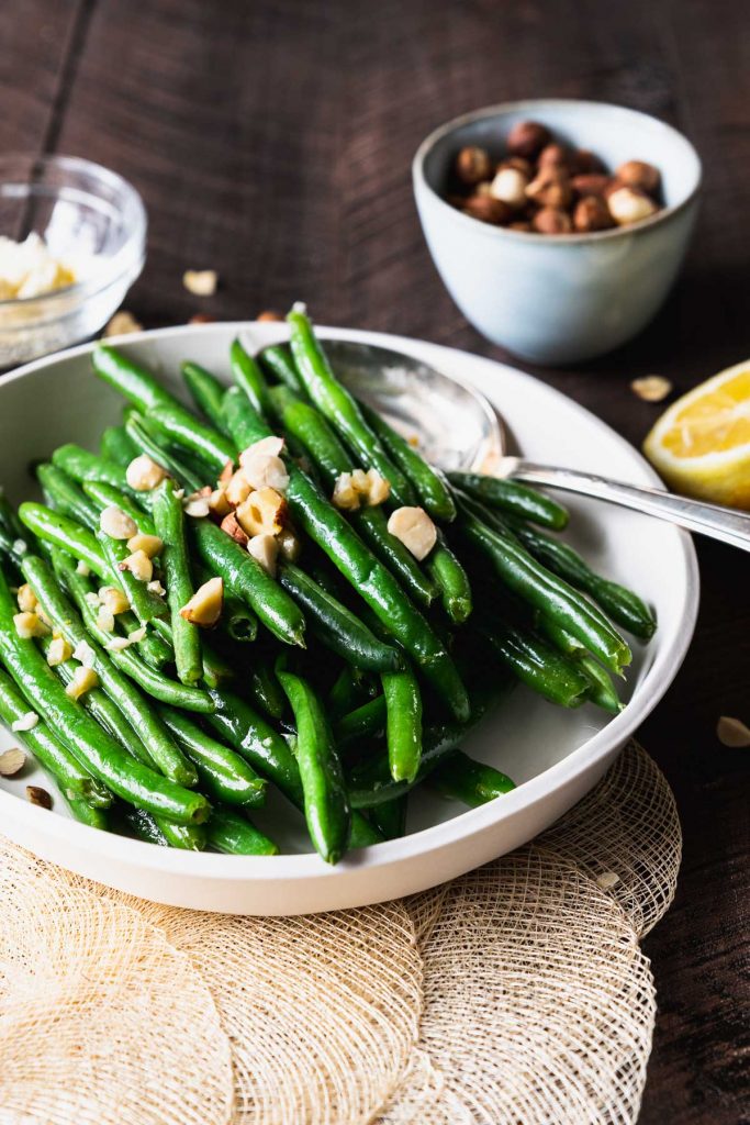 Green beans on a white plate with a silver serving spoon