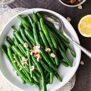 Green beans topped with hazelnut compound butter in a white dish