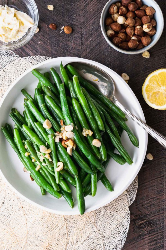 Green beans topped with hazelnut compound butter in a white dish