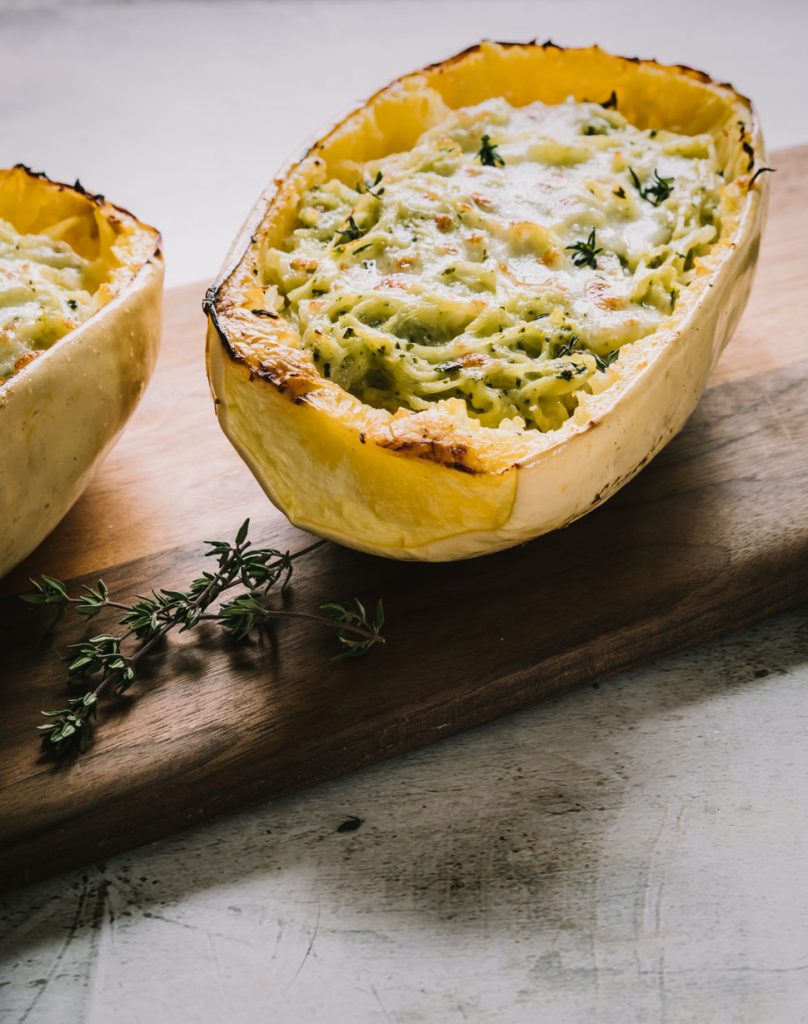 Close up of a half a baked spaghetti squash with cheese and pesto