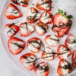 Plate of strawberries stuffed with cheesecake and drizzled with dark chocolate