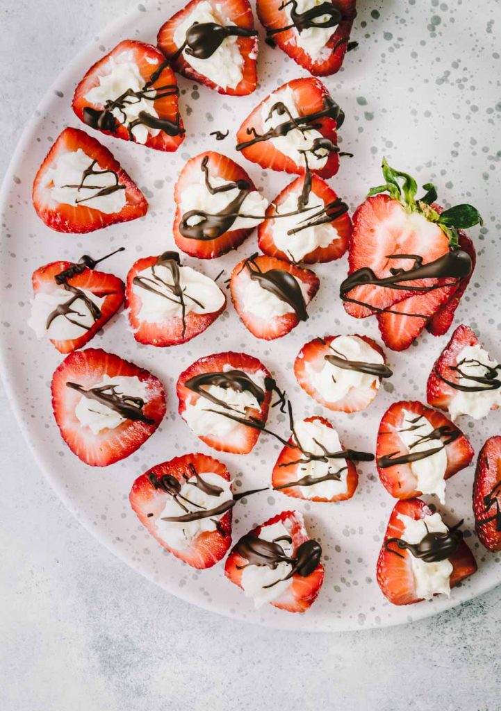 Plate of strawberries stuffed with cheesecake and drizzled with dark chocolate