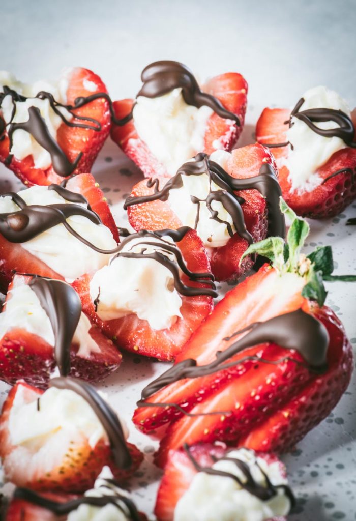 Close up of strawberry halves stuffed with cheesecake and drizzled with dark chocolate