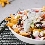 Plate of oven baked french fries topped with tomatoes, peppers, red onion, feta and tzatziki sauce