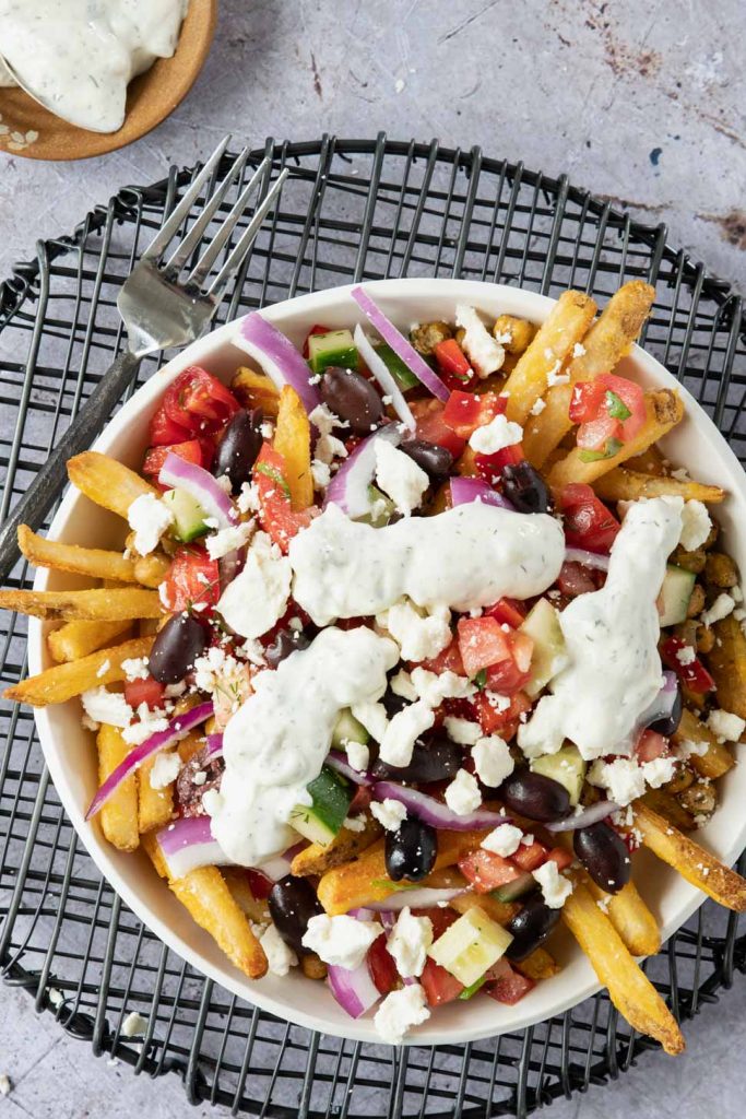Plate of oven baked fries topped with marinated tomatoes, kalamata olives, feta cheese and tzatziki sauce