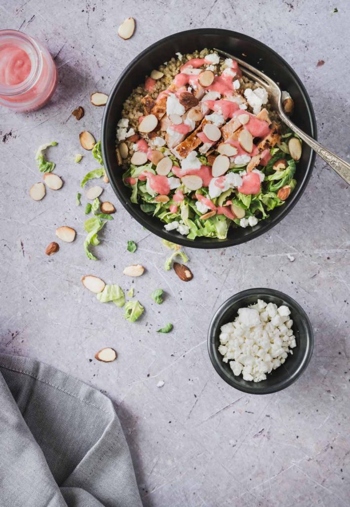 Quinoa in a black bowl topped with grilled chicken, goat cheese and a drizzle of bright pink raspberry dressing