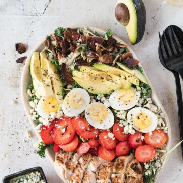 Cobb salad topped with grilled chicken, bacon, avocado, hard boiled eggs and strawberries.