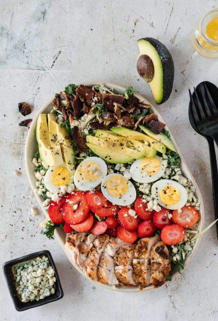 Cobb salad topped with grilled chicken, avocado, bacon and strawberries