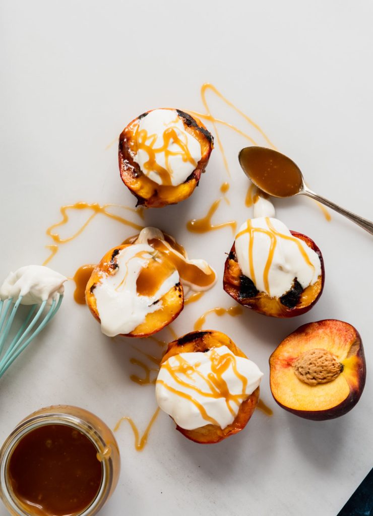 Four grilled peach halves topped with whipped mascarpone and drizzled with caramel sauce