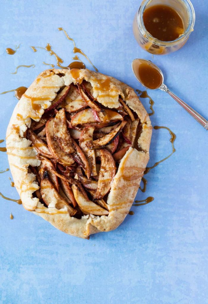 Whole apple galette drizzled with caramel sauce on a blue background