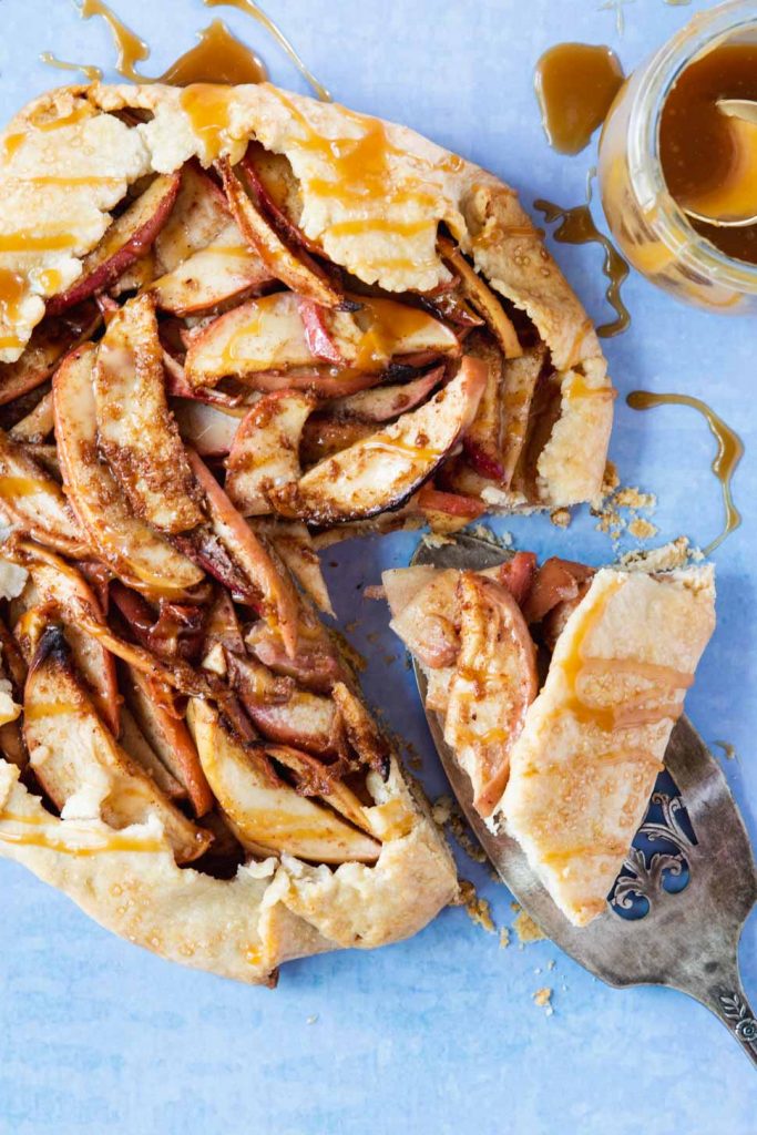 Apple galette on a light blue background with a slice being served