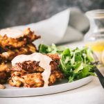 Close up of two crab cakes staked on a plate drizzled with spicy aioli