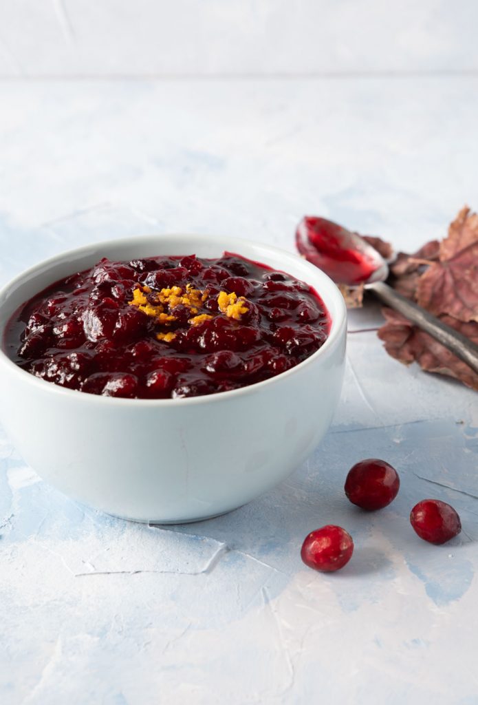Homemade cranberry sauce in a light blue bowl with cranberries scattered around