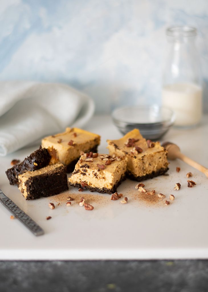 Pumpkin cheesecake bars on a white stone tile dusted with ground nutmeg