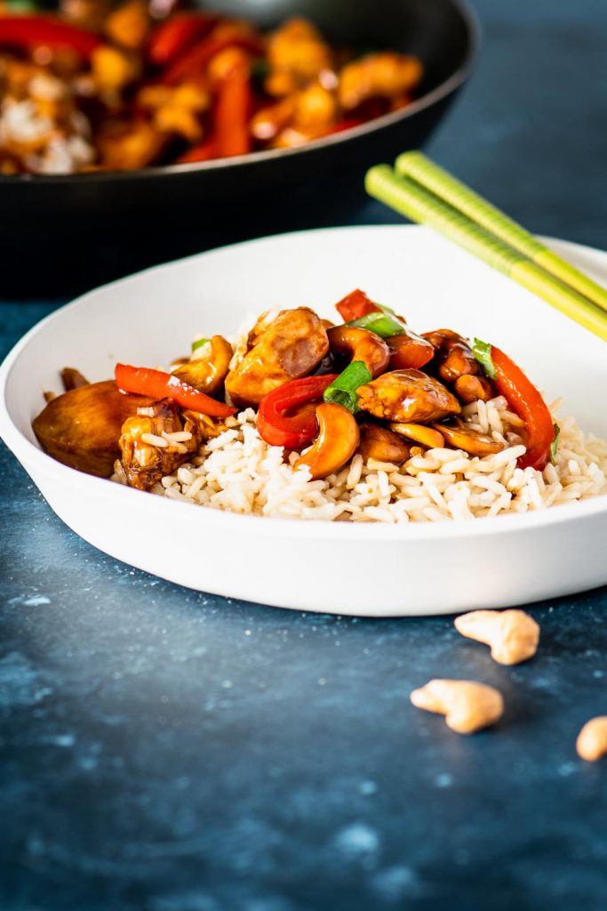 Brown riced topped with cashew chicken stir fry on an off white plate