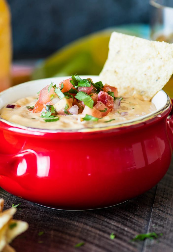 Close up of queso dip topped with pico de gallo with a chip dipped into it