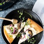 Two slices of ricotta mushroom pizza on a black matte plate shot from overhead