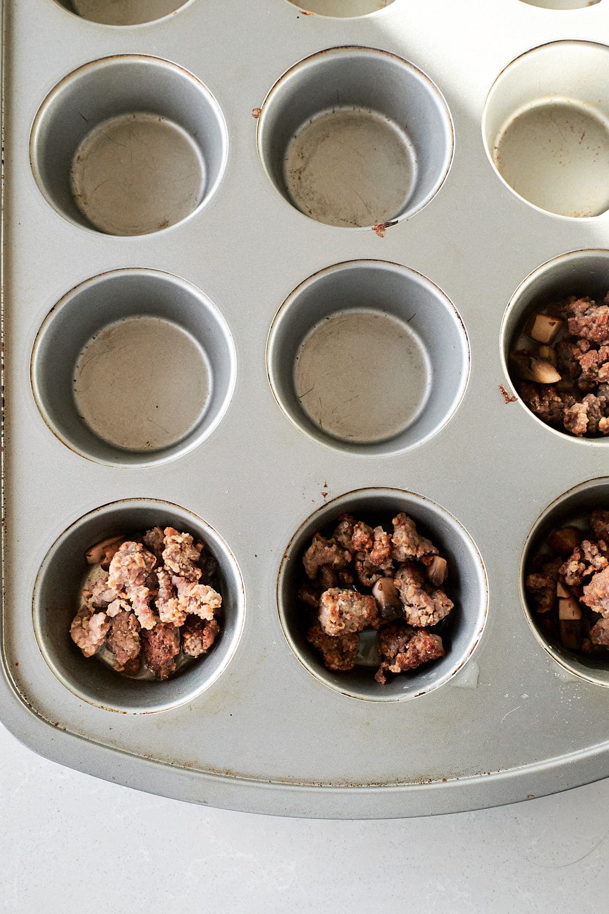 Browned sausage and sauteed mushrooms in a muffin pan cup