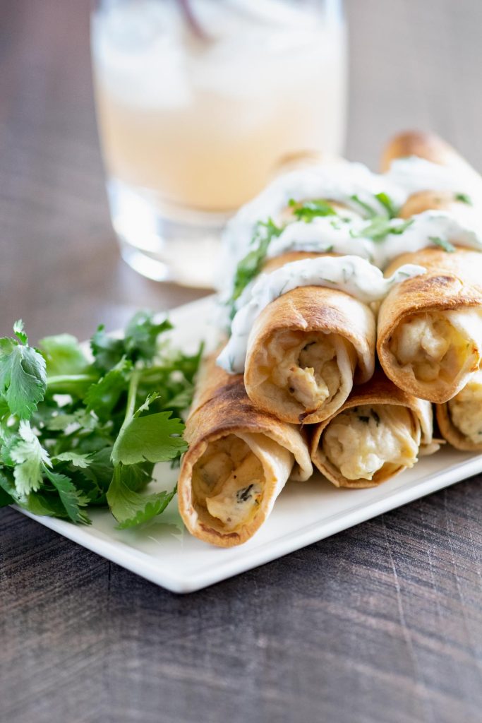 Stack of baked chicken flautas on a white tray