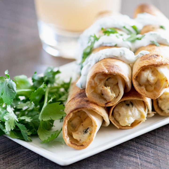 Stack of baked chicken flautas on a white tray