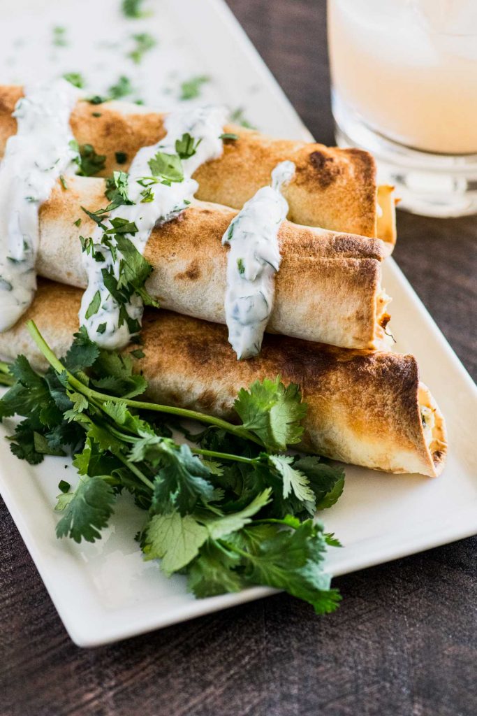 Stack of baked chicken flautas with a margarita in the background