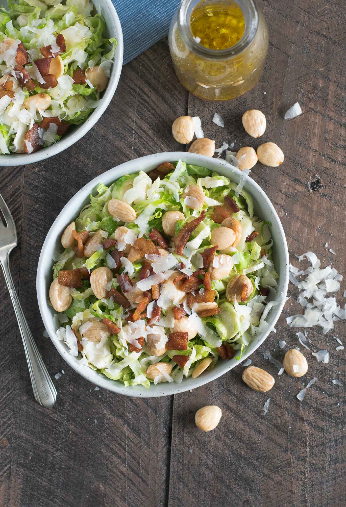 Two bowls of shaved brussels sprouts topped with pancetta, marcona almonds and parmesan