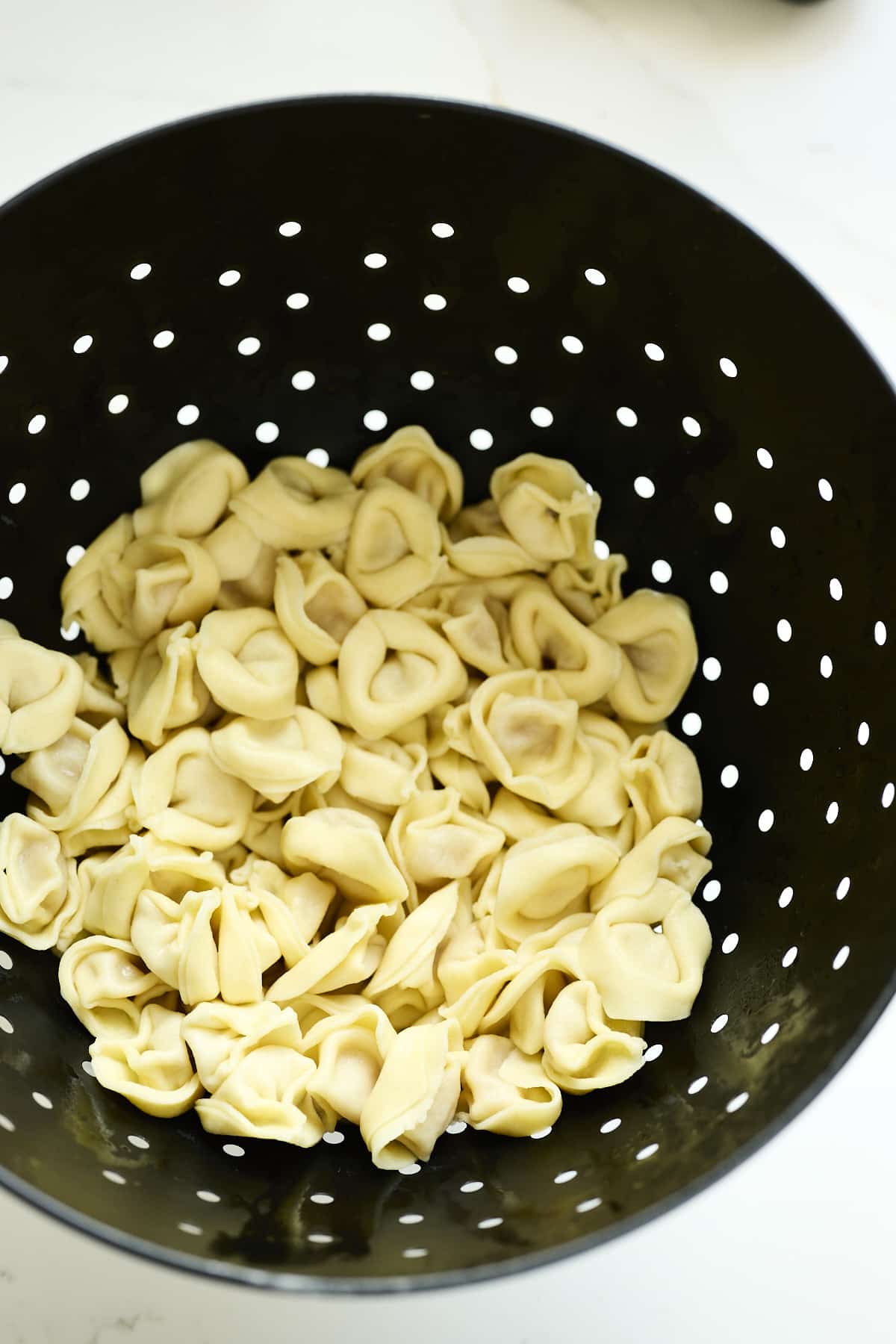 Cooked tortellini in a black strainer