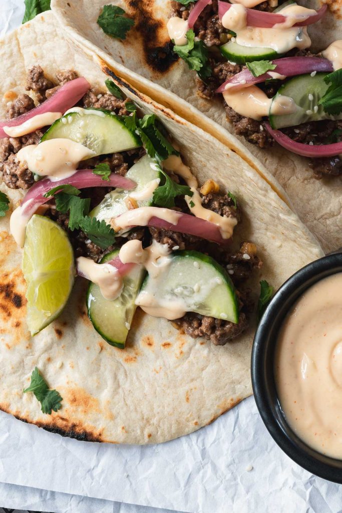 Close up of Korean flavored beef on a flour tortillas topped cucumbers and pickled red onions