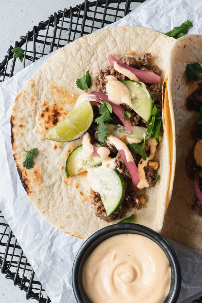 One Korean beef taco on a black round wire rack with a side of spicy mayo