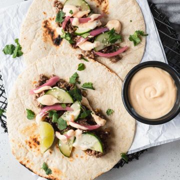 Two flour tortillas topped with Korean ground beef, cilantro and pickled onions