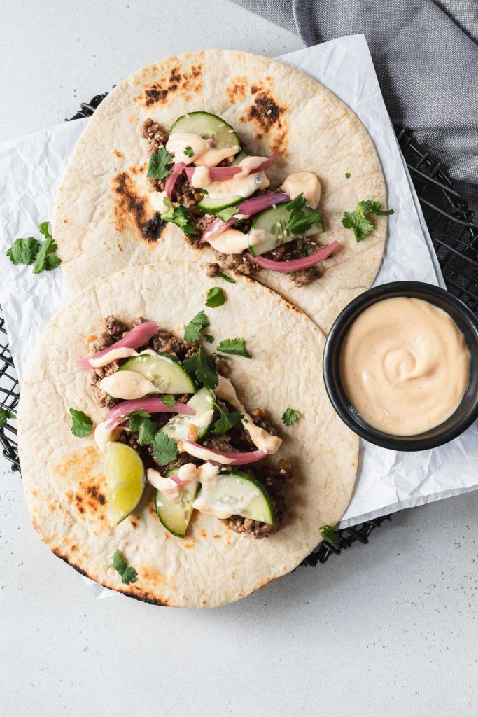 Two flour tortillas topped with Korean ground beef, cilantro and pickled onions