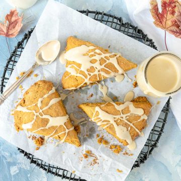 Three pumpkin scones drizzled with glaze on a black wire rack