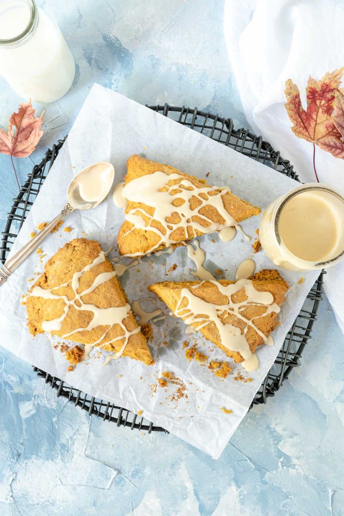 Three pumpkin scones drizzled with glaze on a black wire rack