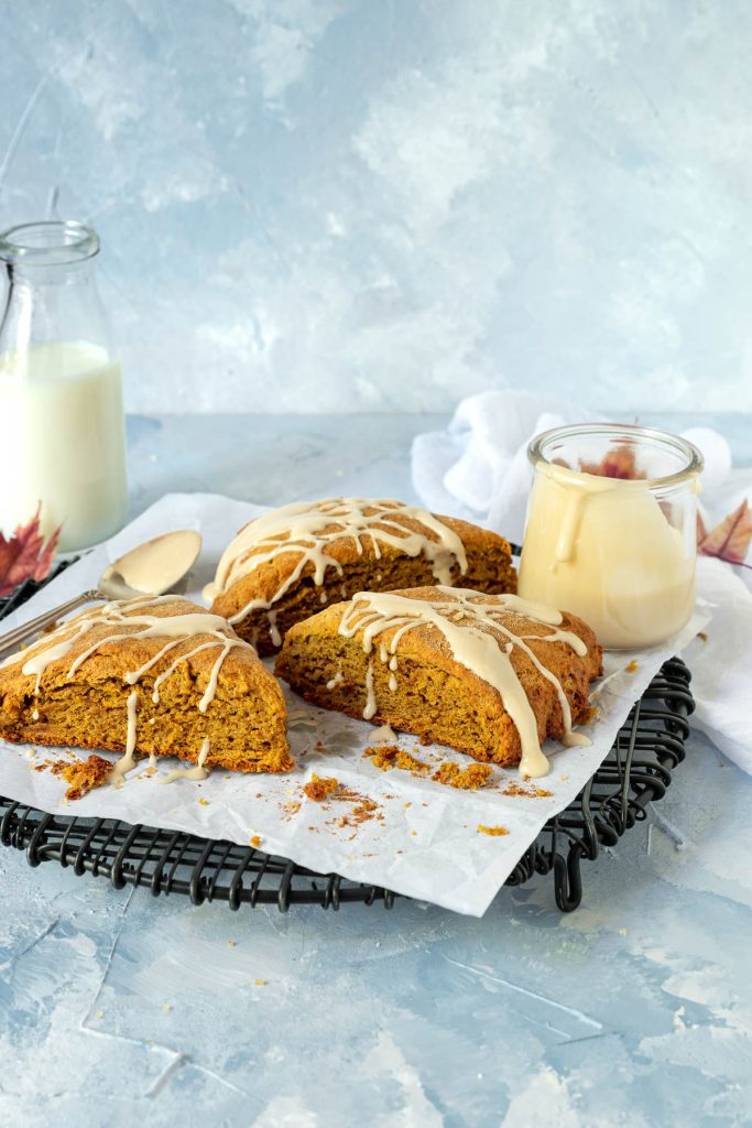 Three pumpkin scones on a black wire cooling rack with a jar of maple glaze on the side