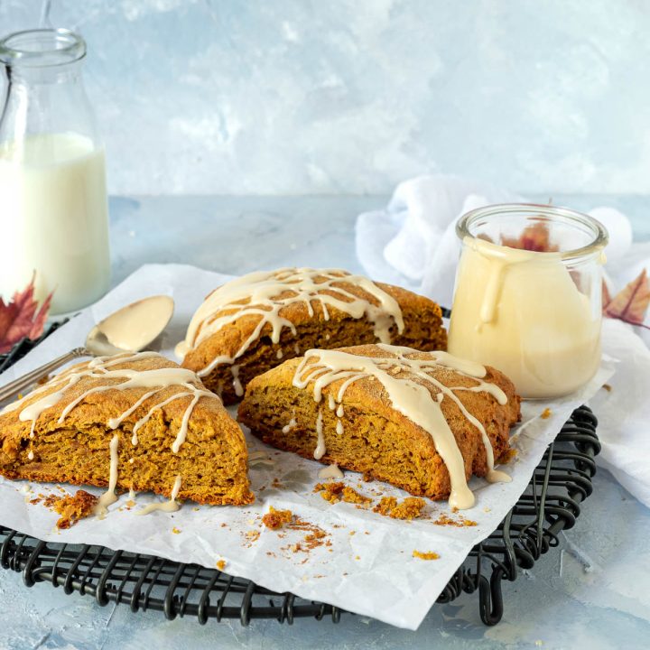 Three pumpkin scones on a black wire cooling rack with a jar of maple glaze on the side