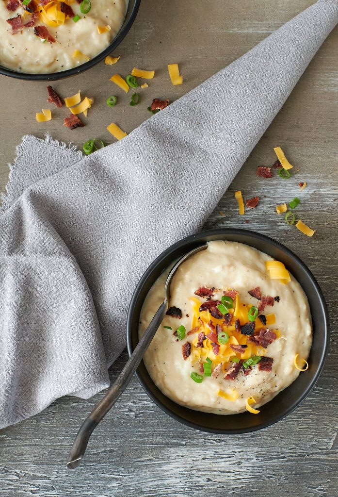 Overhead shot of a black bowl filled with baked potato soup topped with cheese and backon