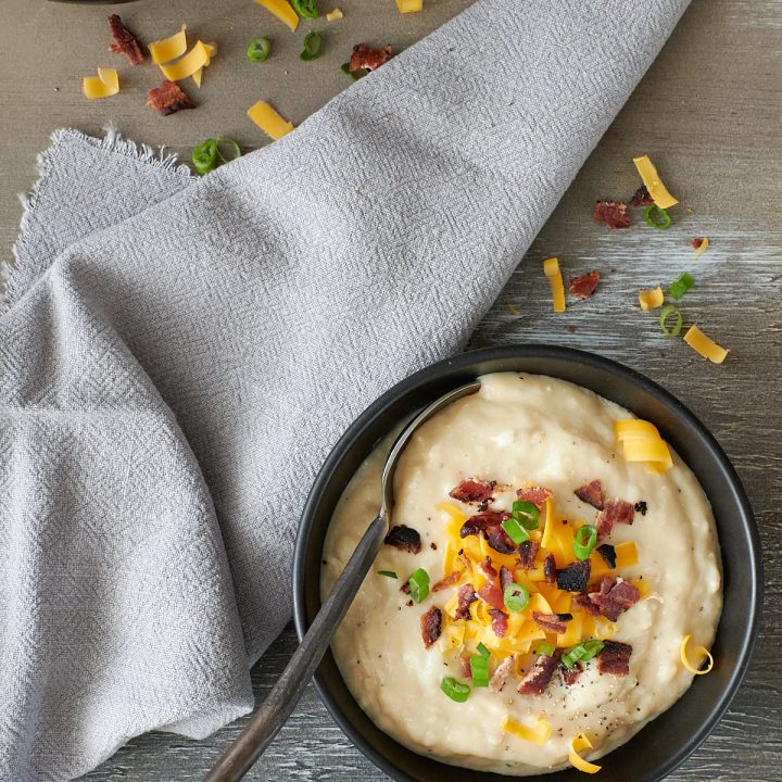 Overhead shot of a black bowl filled with baked potato soup topped with cheese and backon