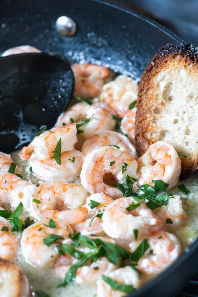 Close up of garlic shrimp in lemon butter with a slice of toasted bread on the side