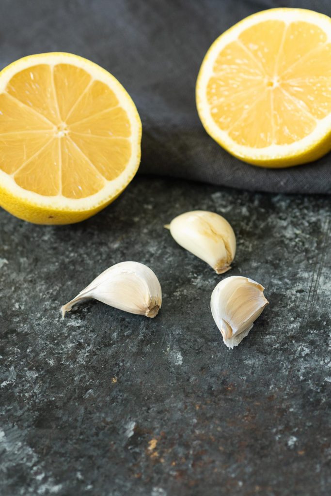 A sliced lemon and three garlic cloves on a dark background