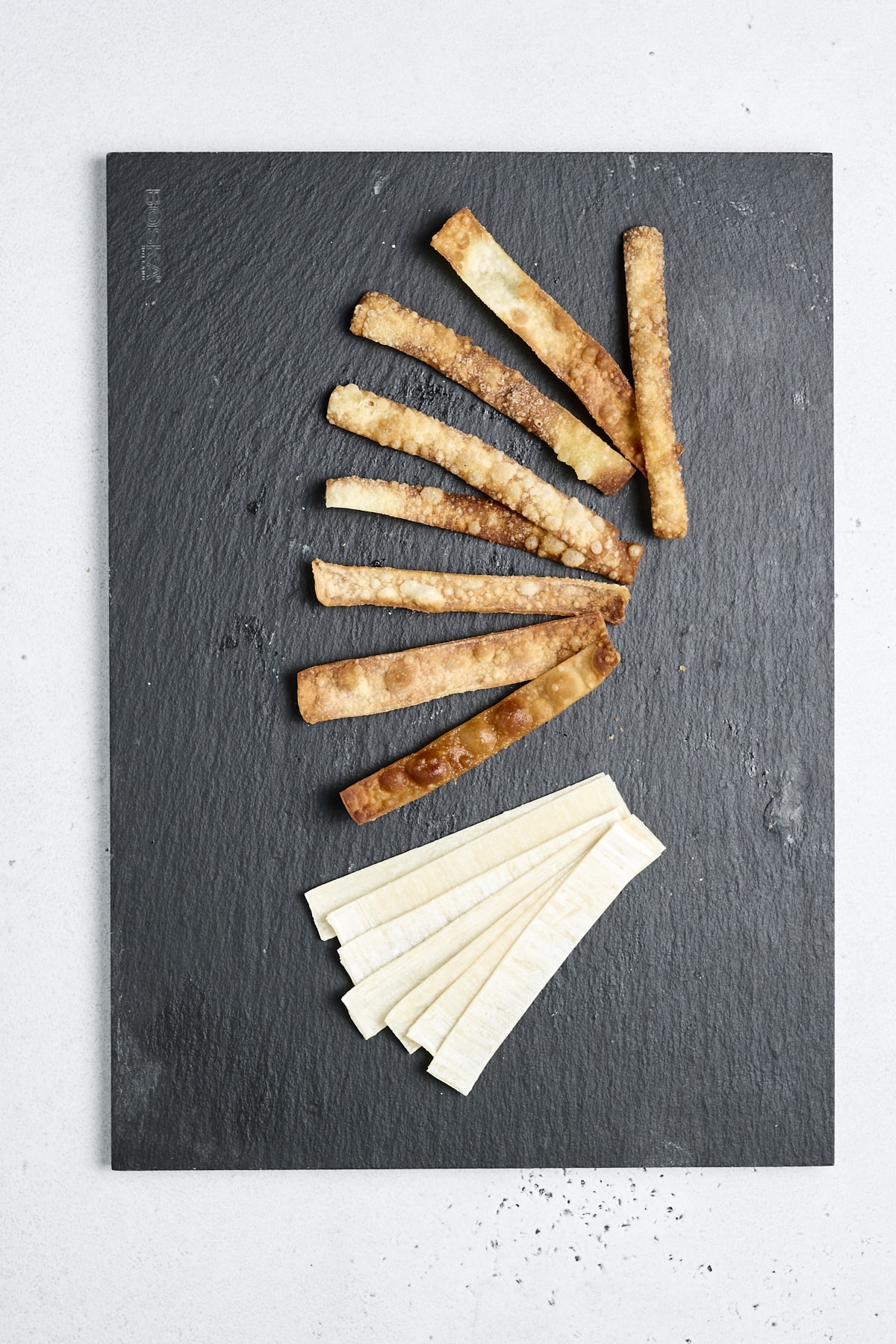Thinly sliced wonton wrappers, some cooked, on a black board