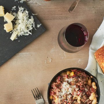 Overhead shot of a small black skillet filled with deconstructed lasagne, with a glass of wine on the side