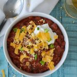 Overhead shot of a bowl of turkey chili topped with shredded cheese, green onions and greek yogurt