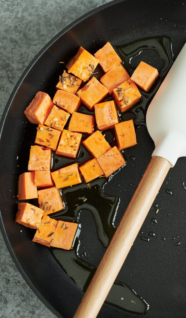 Cubed sweet potatoes cooking in a dark skillet